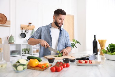 Photo of Smiling man looking at recipe on tablet while cooking at table in kitchen