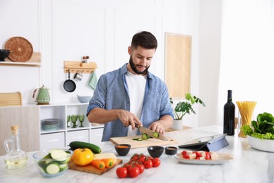 Photo of Cooking process. Young man cutting cucumber at table in kitchen