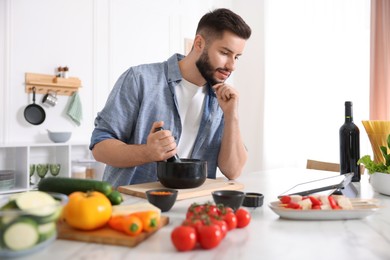 Photo of Young man looking at recipe on tablet while cooking at table in kitchen