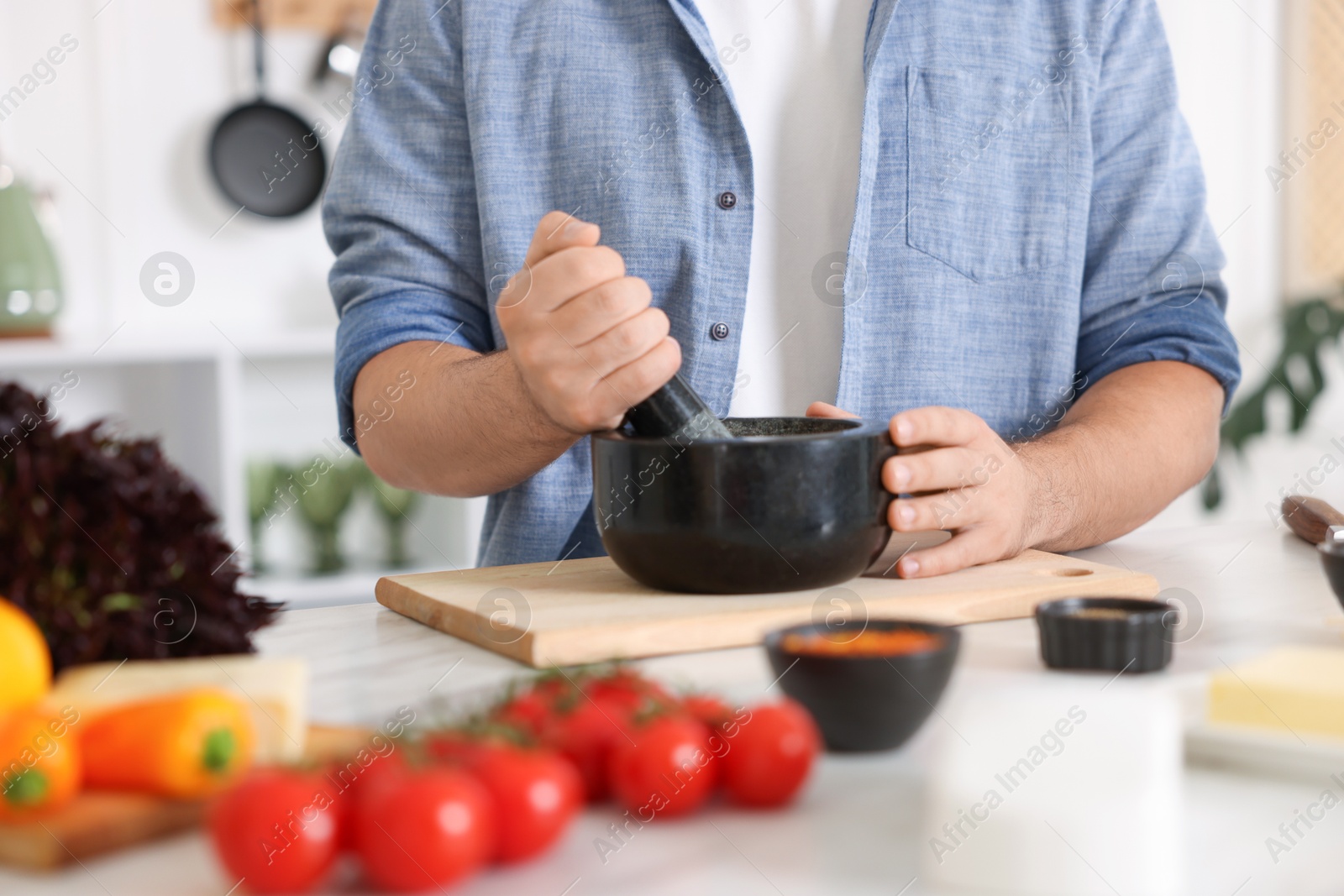 Photo of Man with mortar cooking at table indoors, closeup