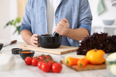 Photo of Man with mortar cooking at table indoors, closeup