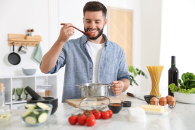 Photo of Smiling man tasting meal after cooking at table in kitchen