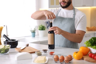 Photo of Man opening bottle of wine while cooking at table in kitchen, closeup