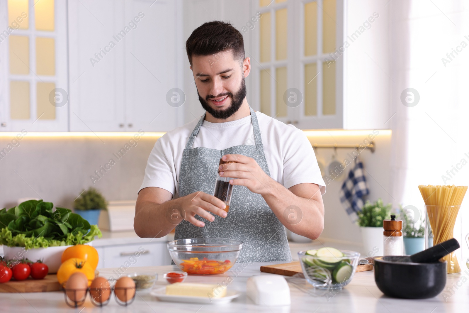 Photo of Cooking process. Smiling man seasoning dish at table in kitchen