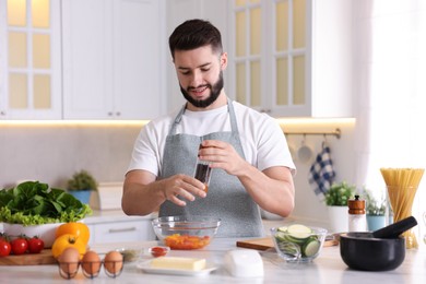 Photo of Cooking process. Smiling man seasoning dish at table in kitchen