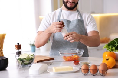 Photo of Cooking process. Smiling man seasoning dish at table in kitchen, closeup