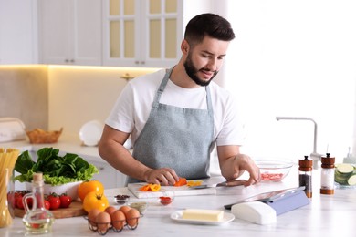 Photo of Young man looking at recipe on tablet while cooking at table in kitchen
