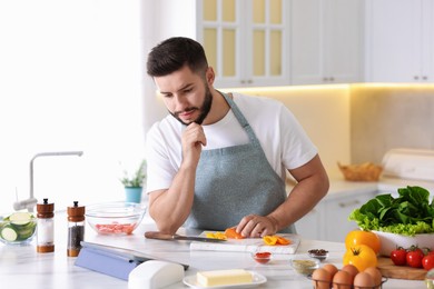 Photo of Young man looking at recipe on tablet while cooking at table in kitchen