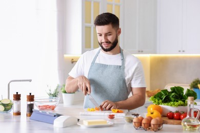 Photo of Smiling man looking at recipe on tablet while cooking at table in kitchen