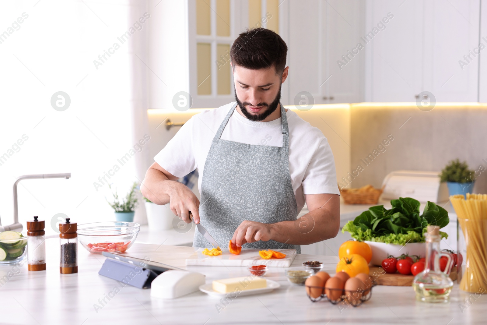Photo of Cooking process. Young man cutting bell pepper at table in kitchen