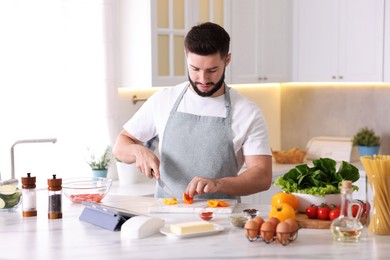 Photo of Cooking process. Young man cutting bell pepper at table in kitchen