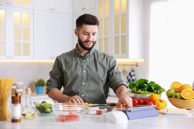 Photo of Smiling man looking at recipe on tablet while cooking at table in kitchen