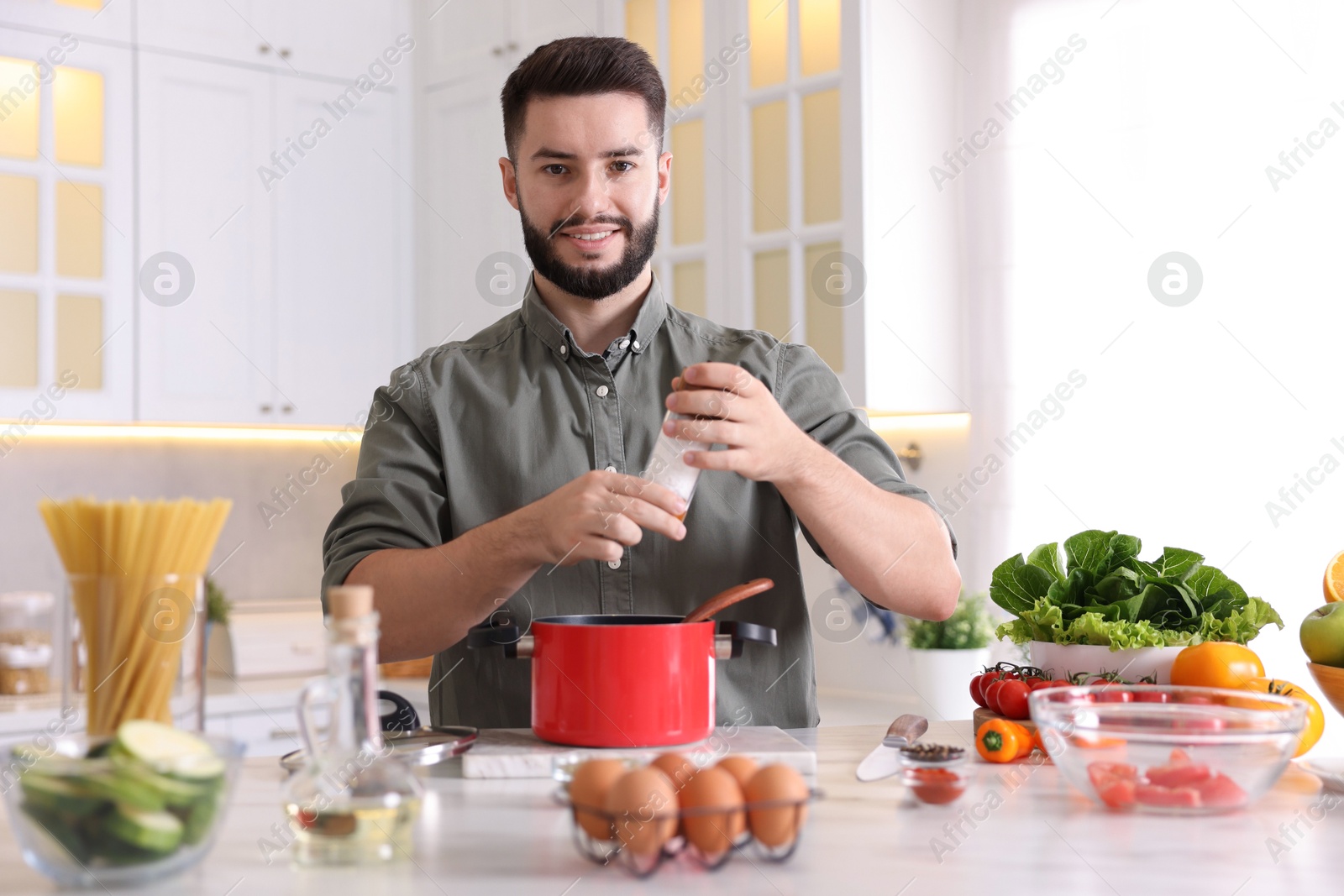 Photo of Cooking process. Smiling man seasoning dish at table in kitchen