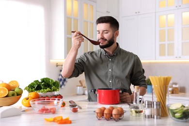 Photo of Smiling man tasting meal after cooking at table in kitchen