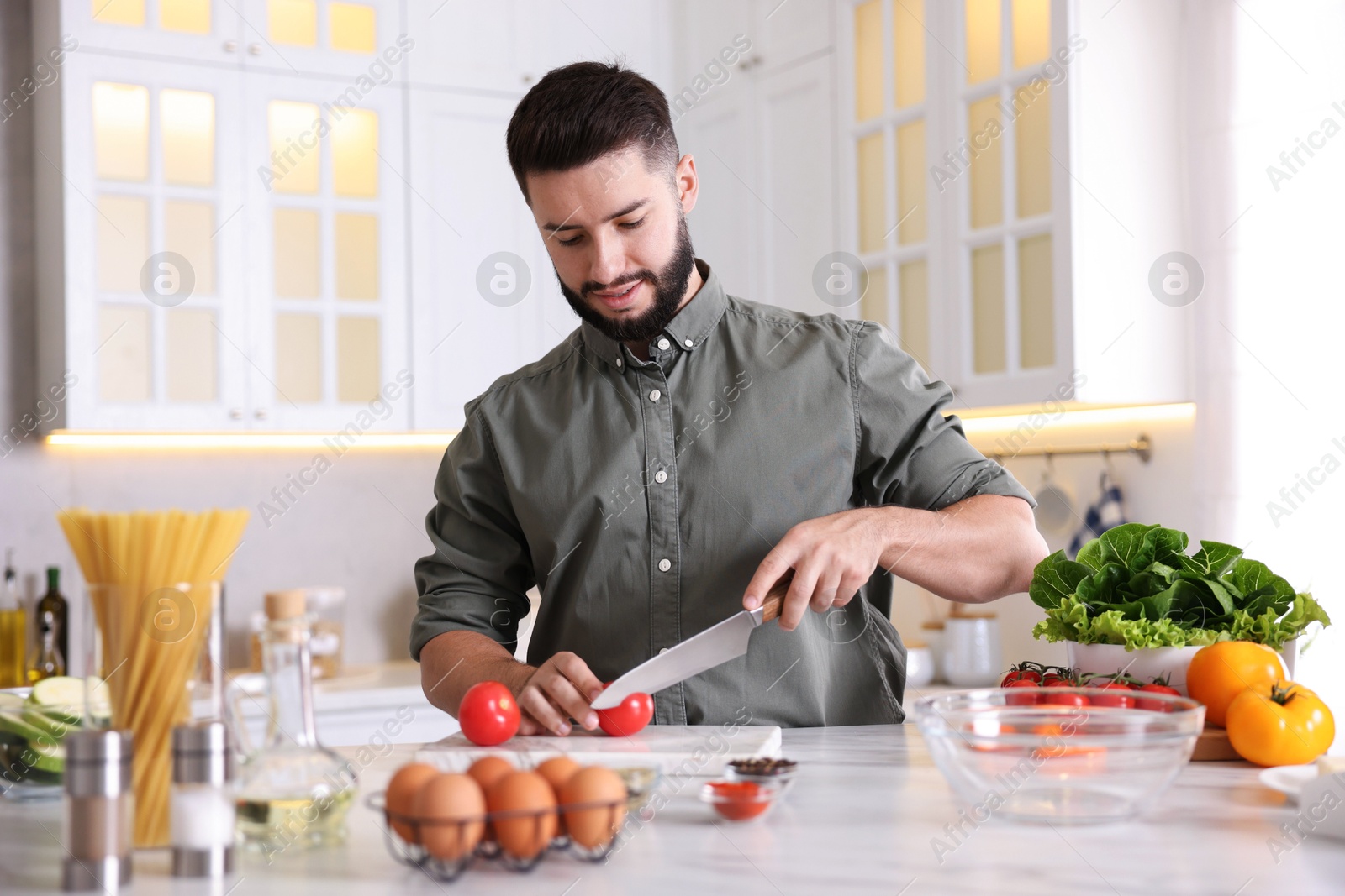 Photo of Cooking process. Smiling man cutting tomato at table in kitchen
