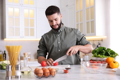 Photo of Cooking process. Smiling man cutting tomato at table in kitchen