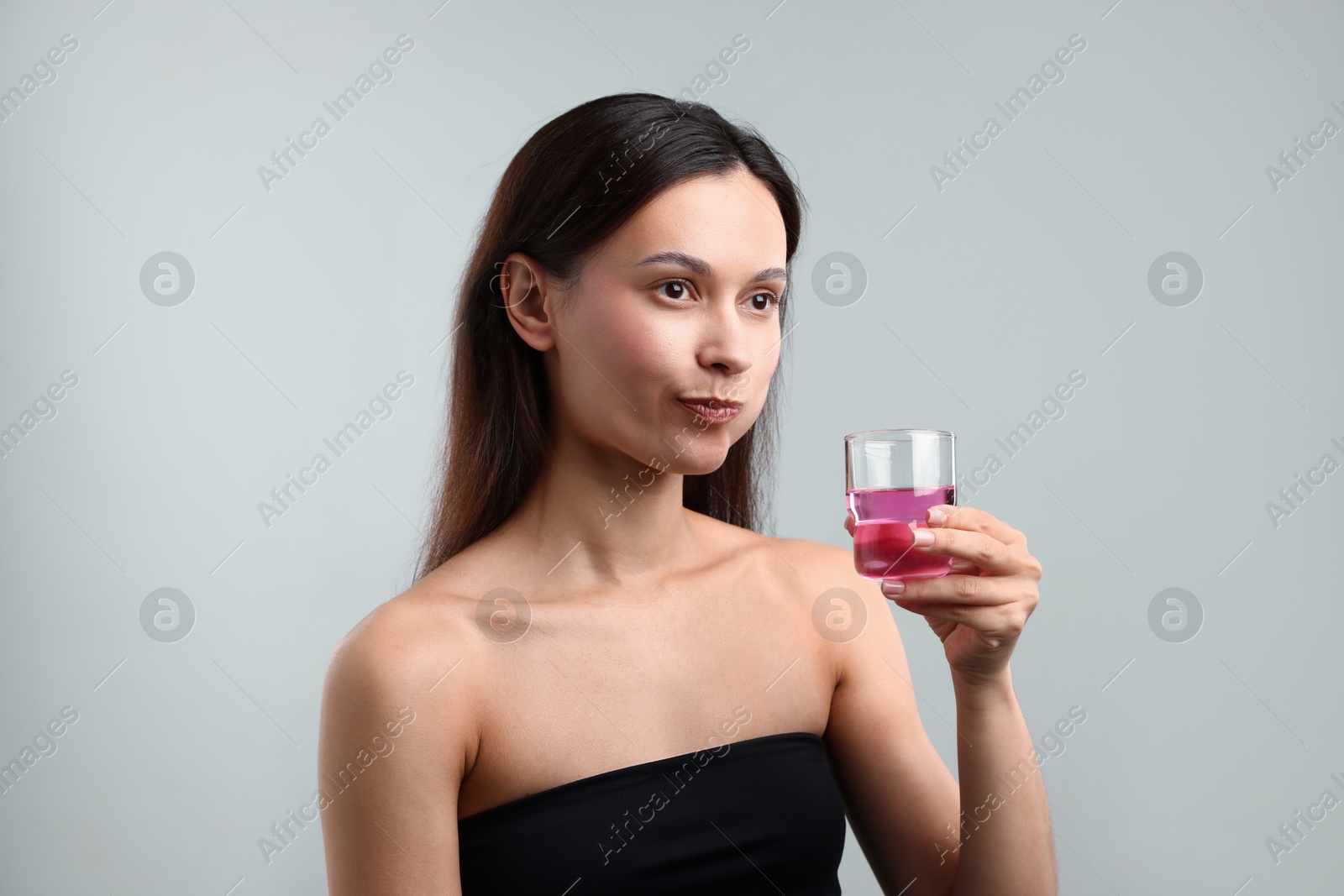 Photo of Young woman rinsing mouth with mouthwash on grey background. Oral hygiene