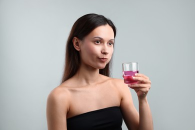 Photo of Young woman rinsing mouth with mouthwash on grey background. Oral hygiene