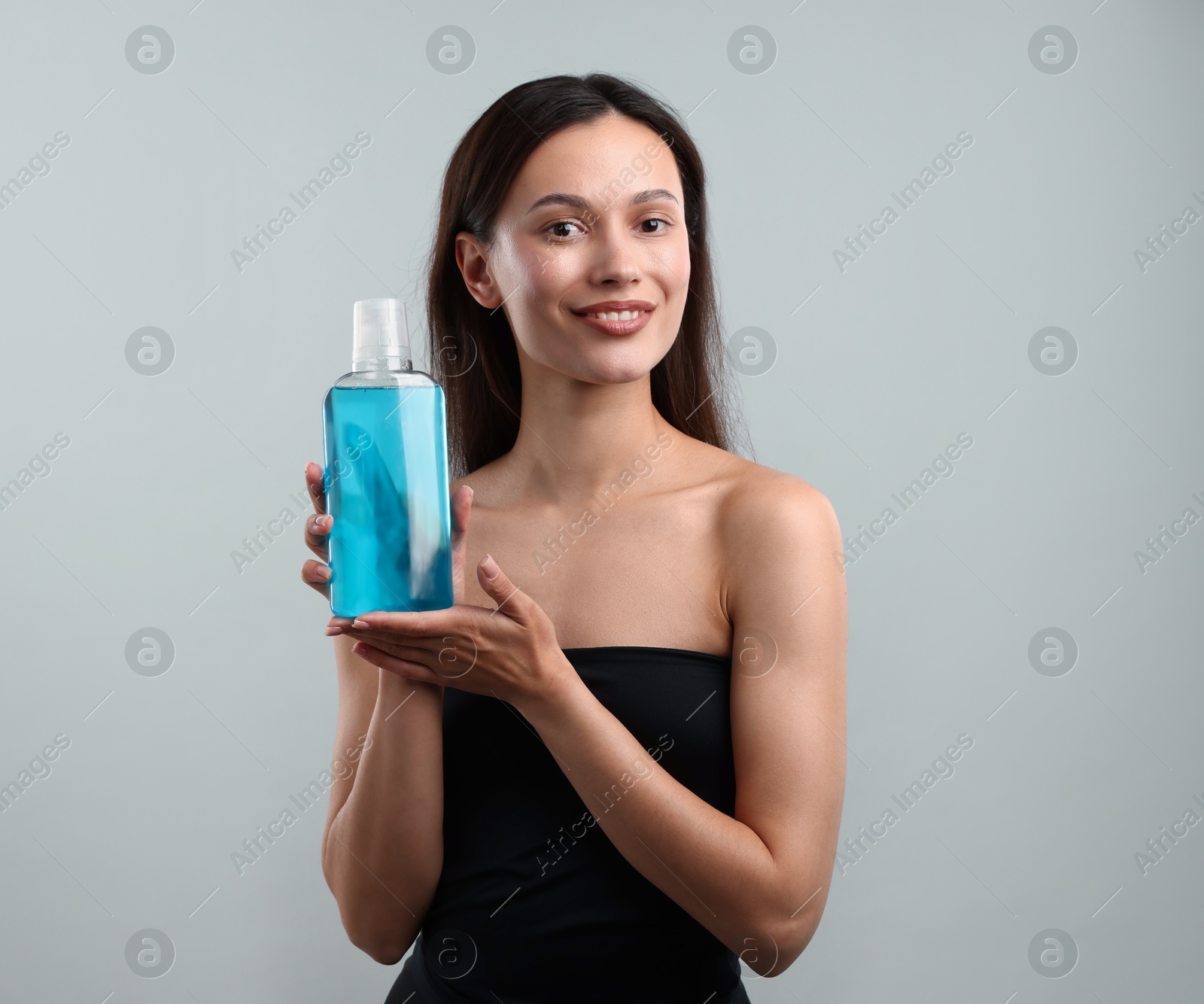 Photo of Smiling young woman with bottle of mouthwash on grey background. Oral hygiene