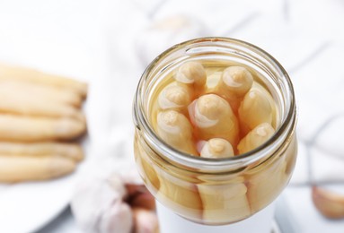 Photo of Pickled asparagus in jar on white table, closeup