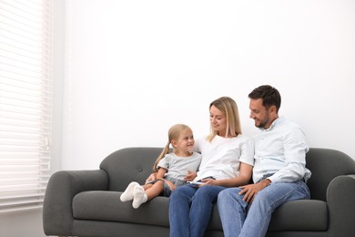 Photo of Happy family with air conditioner remote control on sofa at home. Space for text