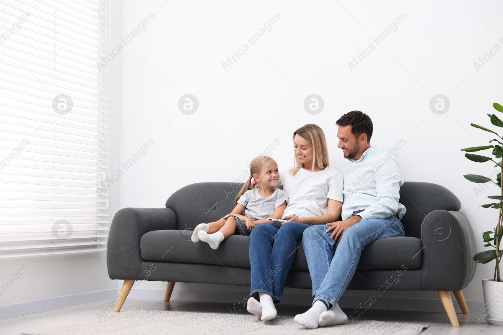 Photo of Happy family with air conditioner remote control on sofa at home. Space for text