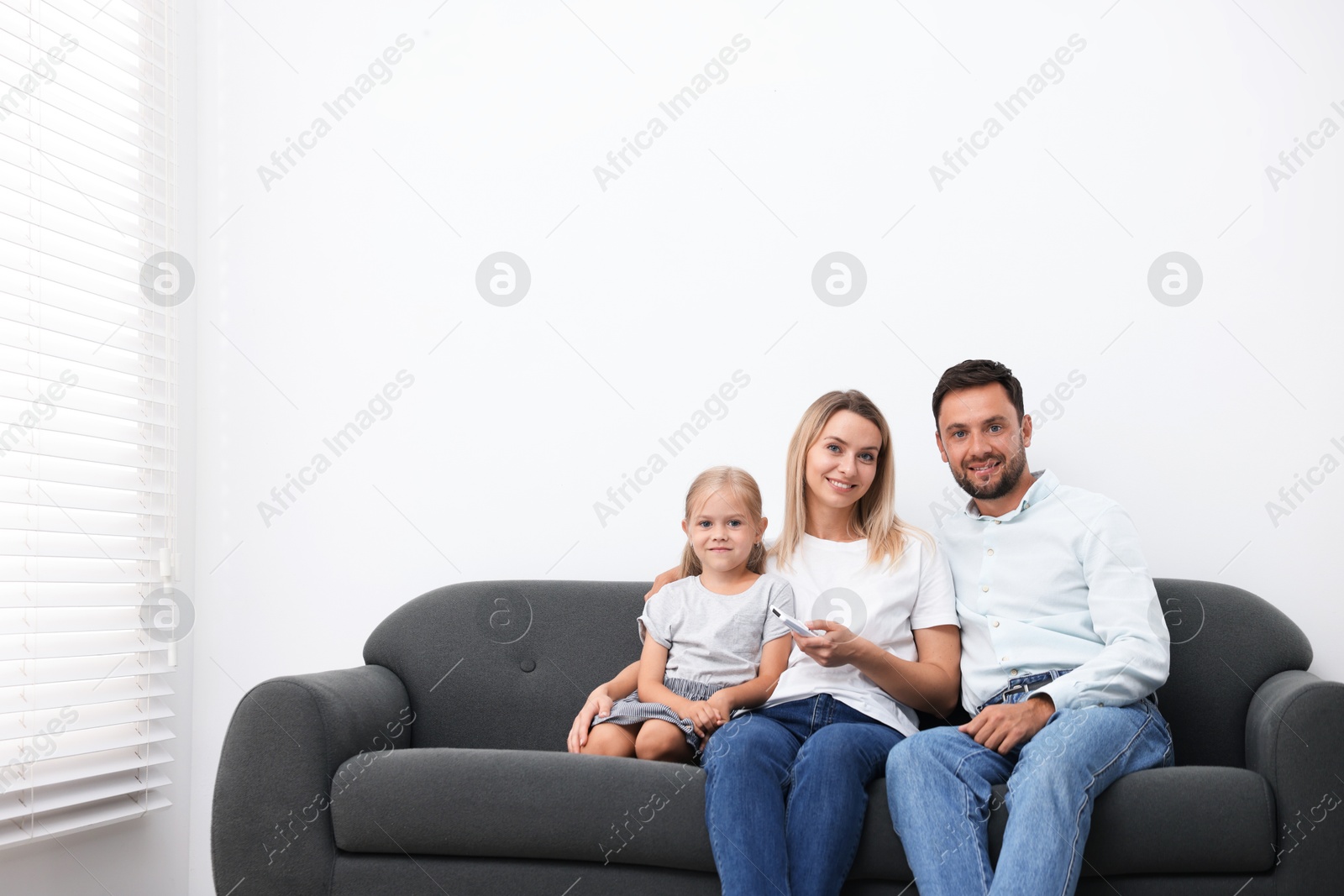Photo of Happy family using remote to control air conditioner on sofa at home. Space for text