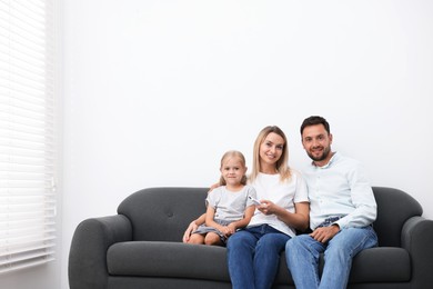 Photo of Happy family using remote to control air conditioner on sofa at home. Space for text
