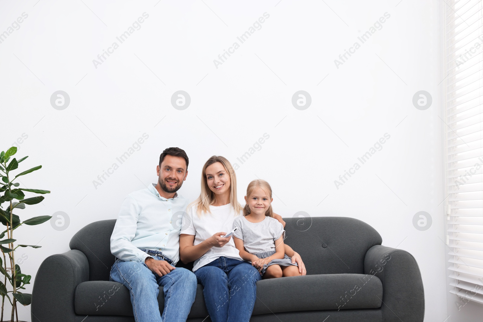 Photo of Happy family using remote to control air conditioner on sofa at home. Space for text