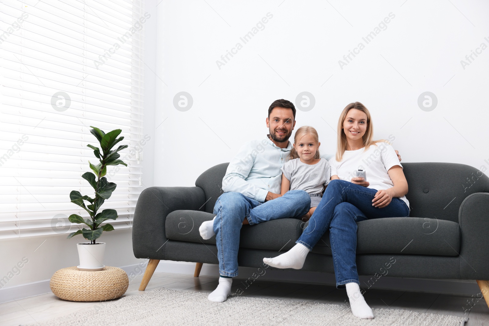 Photo of Happy family with air conditioner remote control on sofa at home
