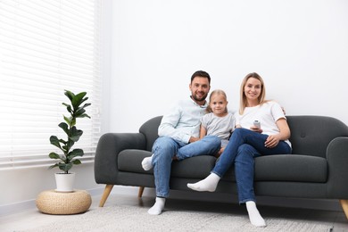Photo of Happy family with air conditioner remote control on sofa at home