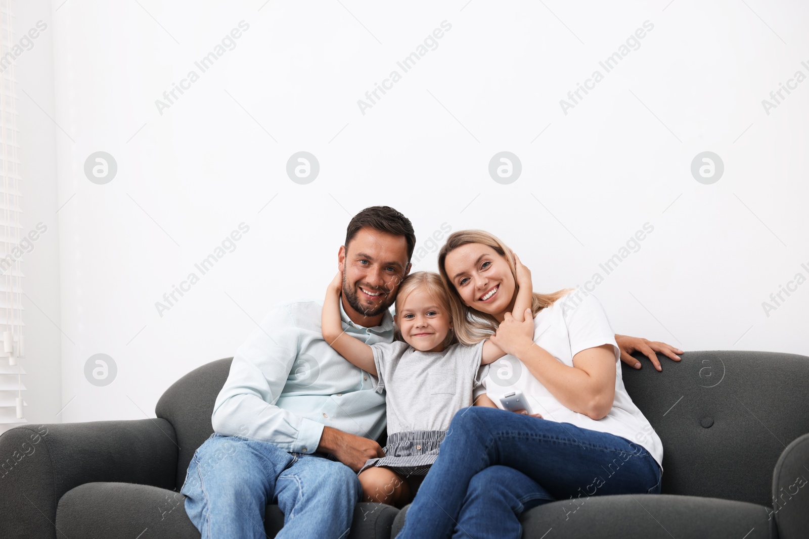 Photo of Happy family with air conditioner remote control on sofa at home