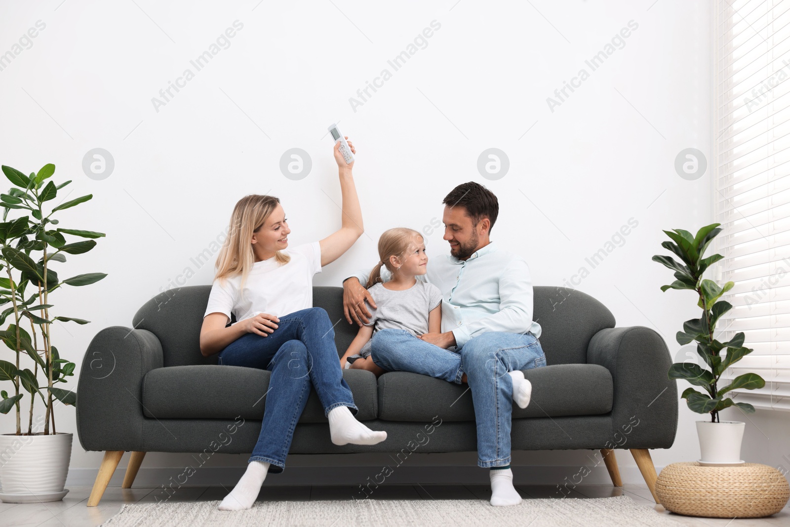 Photo of Happy family using remote to control air conditioner on sofa at home