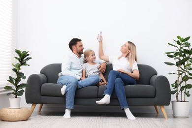 Photo of Happy family using remote to control air conditioner on sofa at home