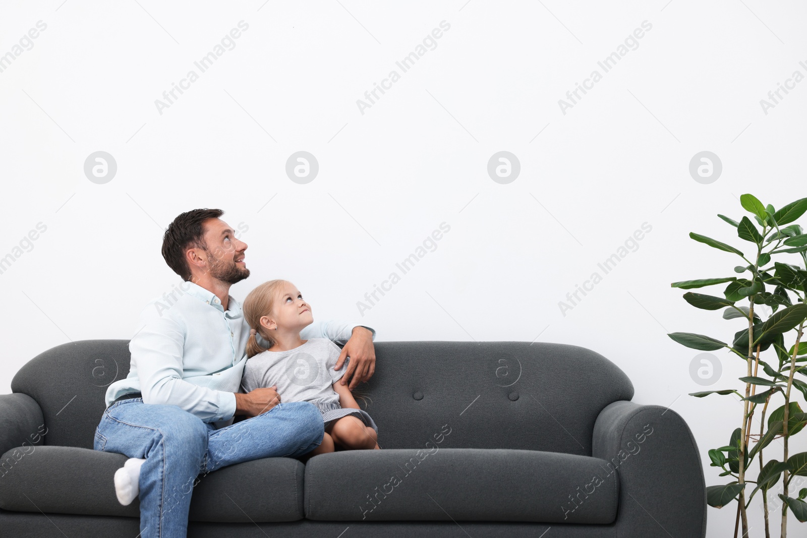 Photo of Father and daughter spending time together on sofa at home. Space for text