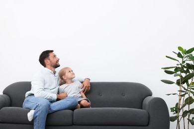 Photo of Father and daughter spending time together on sofa at home. Space for text