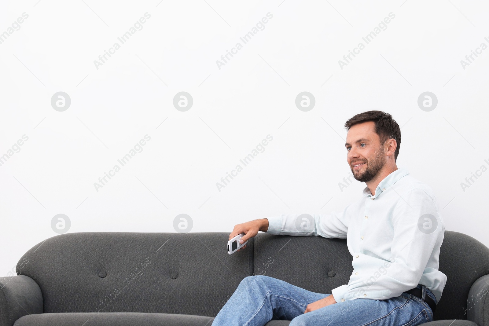 Photo of Man with air conditioner remote control on sofa at home. Space for text