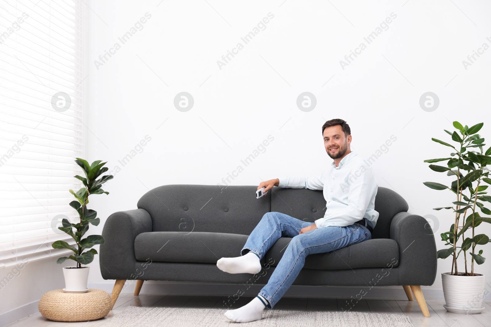 Photo of Man with air conditioner remote control on sofa at home. Space for text