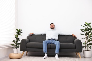 Photo of Man with air conditioner remote control on sofa at home