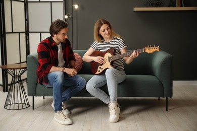 Photo of Tutor teaching woman to play guitar on sofa at home