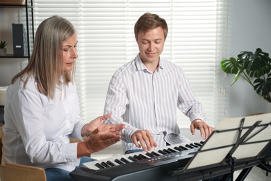 Photo of Tutor teaching man to play piano indoors