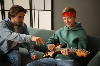 Photo of Tutor teaching man to play guitar on sofa indoors