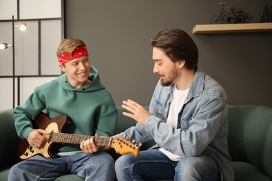 Photo of Tutor teaching man to play guitar on sofa indoors