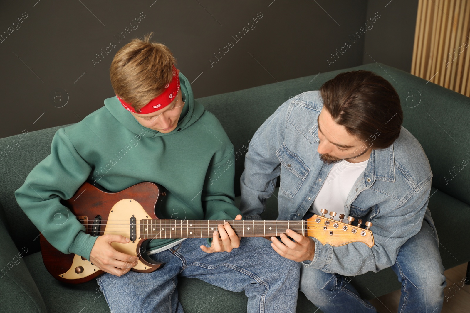 Photo of Tutor teaching man to play guitar on sofa indoors
