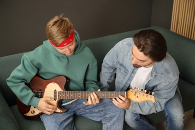 Photo of Tutor teaching man to play guitar on sofa indoors
