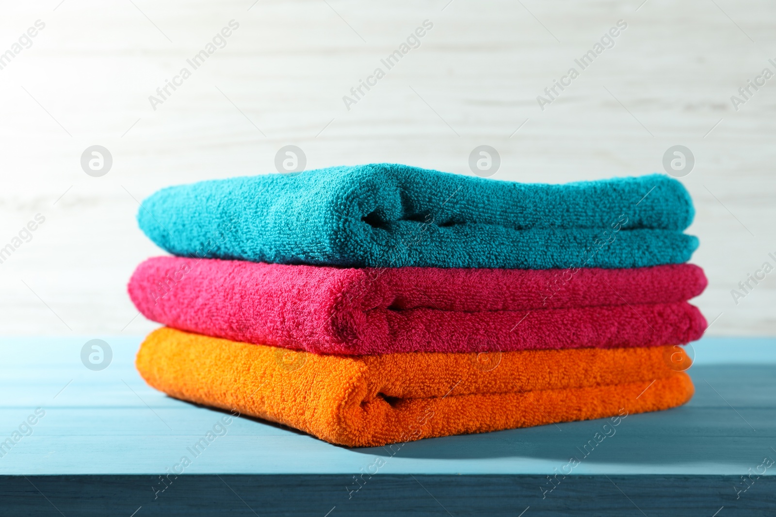 Photo of Colorful fresh terry towels on blue wooden table against white background, closeup