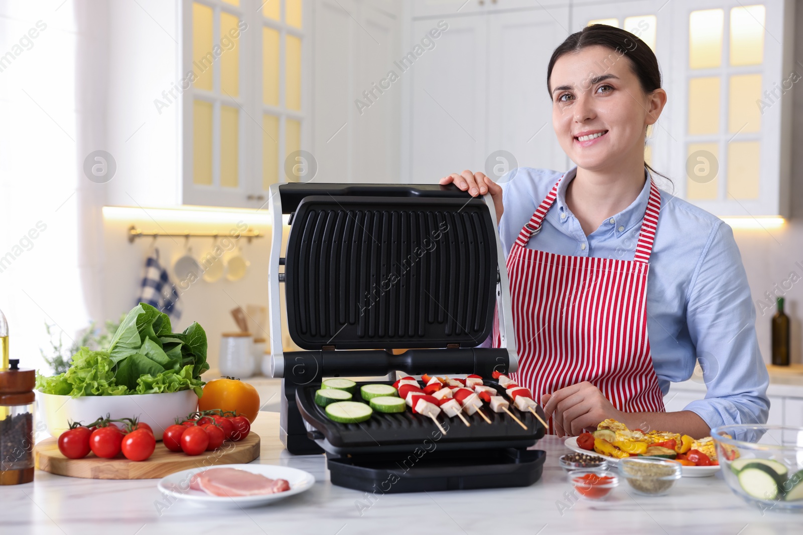 Photo of Woman cooking skewers with meat and vegetables on electric grill at home