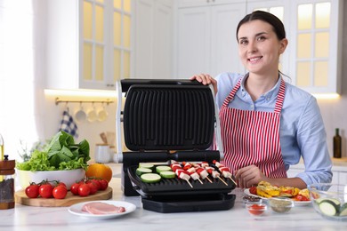 Photo of Woman cooking skewers with meat and vegetables on electric grill at home