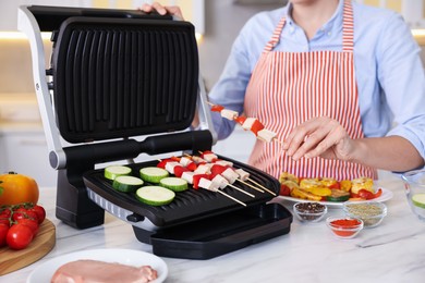 Photo of Woman cooking skewers with meat and vegetables on electric grill at home, closeup