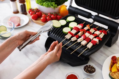 Photo of Woman cooking skewers with meat and vegetables on electric grill at home, closeup